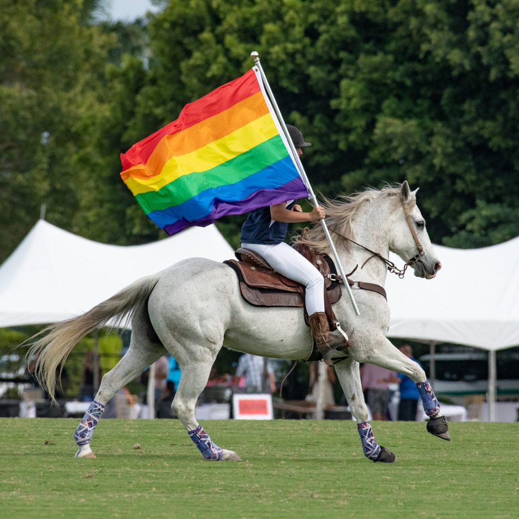 Jockey riding a horse carrying a gay pride flag