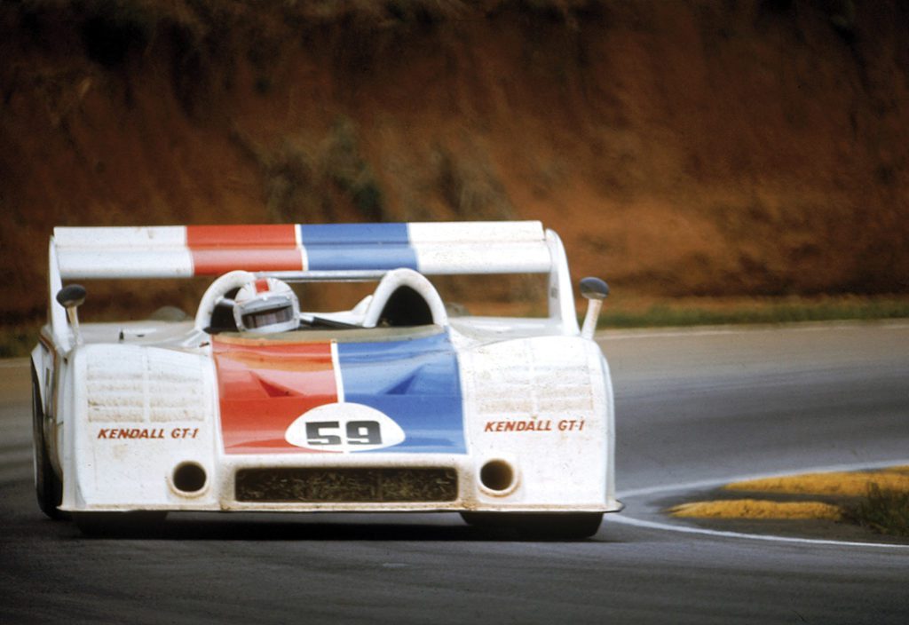 Haywood behind the wheel of a 917-10 Porsche Spyder, a low, boxy car. It is white with a blue and red stripe.